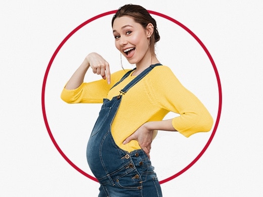 Lykkelig ung, gravid kvinde i gul bluse, der peger på sin mave