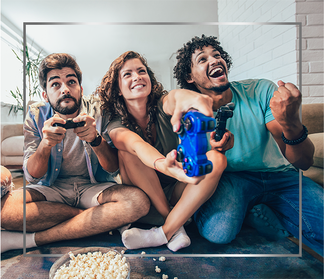 En gruppe unge, smilende mennesker, der sidder på gulvet og spiller videospil og er glade efter Canesten® behandling mod svampeinfektion i huden